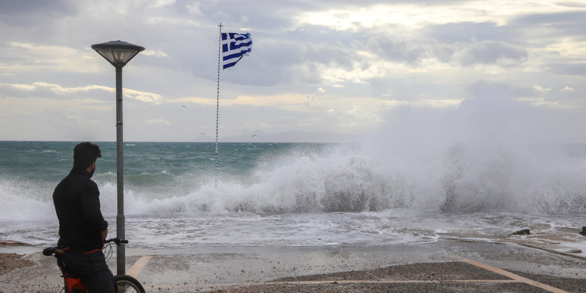 Σημαία της Ελλάδας σε παραλία με φουρτουνιασμένη θάλασσα