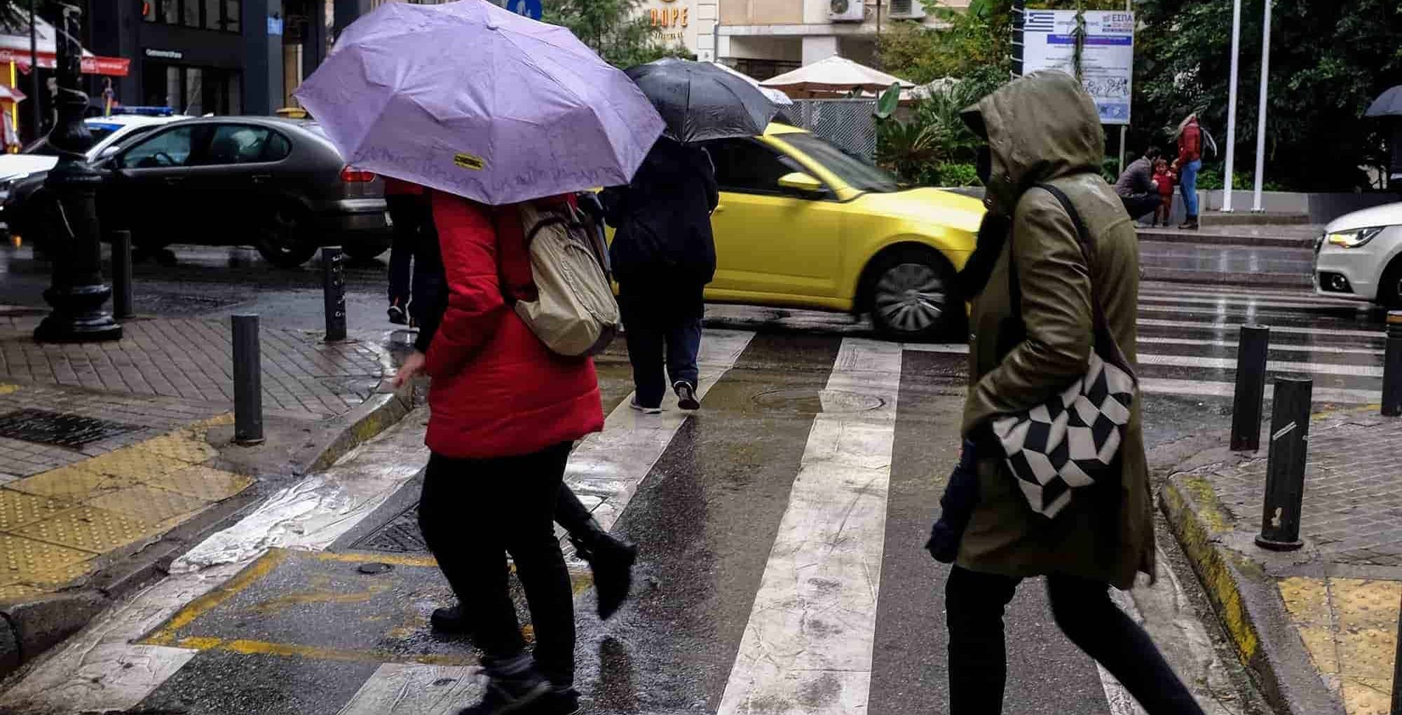 Πολίτες περπατούν με ομπρέλες στο κέντρο της Αθήνας