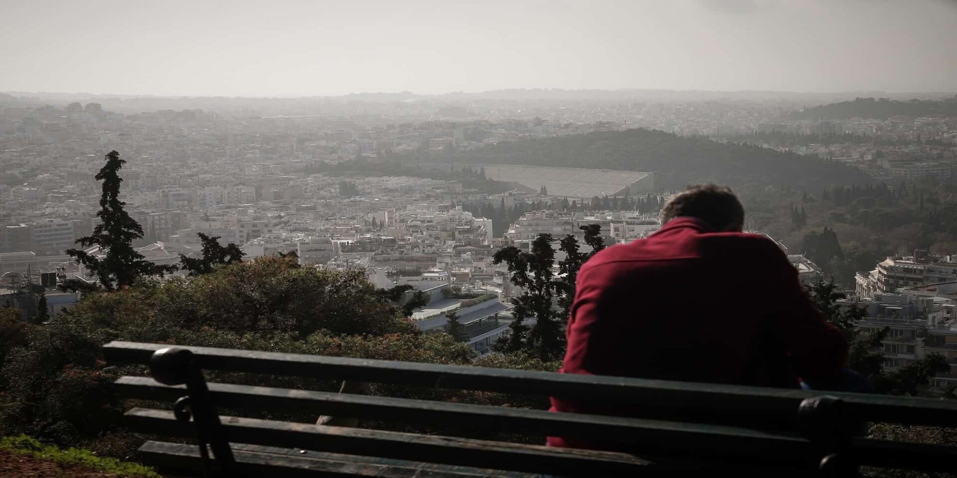 Πολίτης κάθεται σε παγκάκι στην Αττική με περιορισμένη θέα, λόγω της αφρικανικής σκόνης