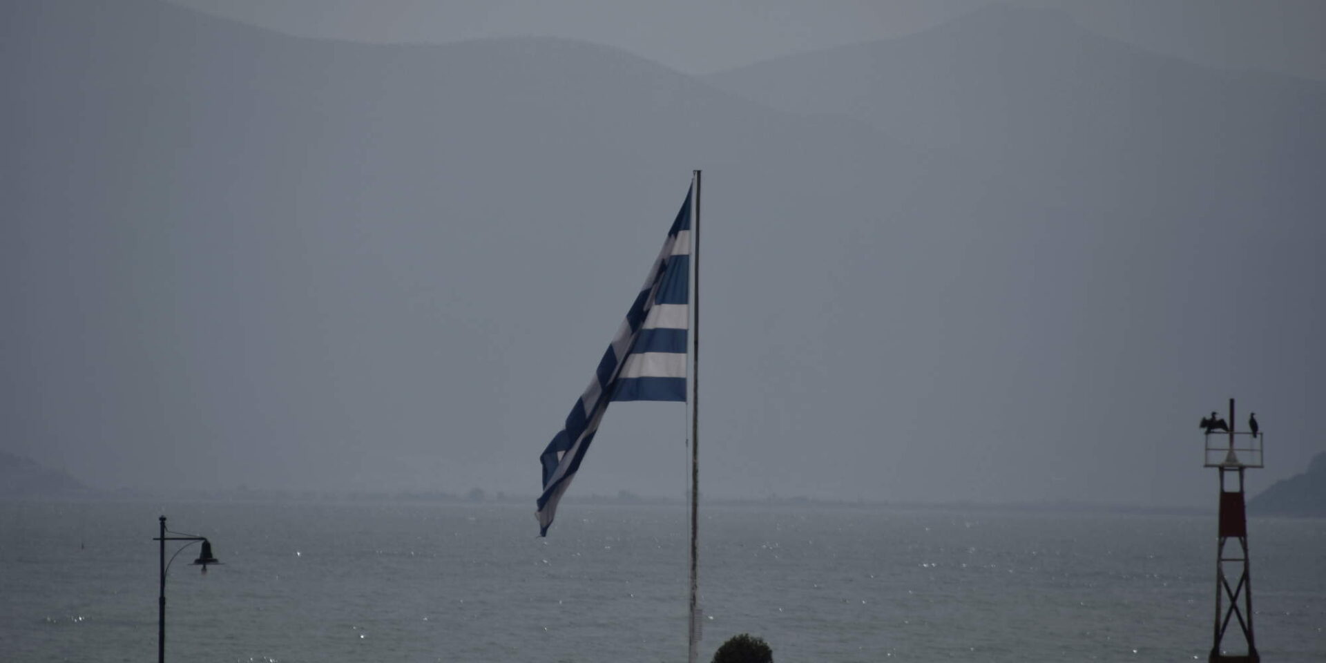 Ο καιρός αυτές τις ημέρες διακρίνεται από χαμηλή ορατότητα λόγω αφρικανικής σκόνης. Η σημαία με φόντο τη θάλασσα στο παραλιακό μέτωπο
