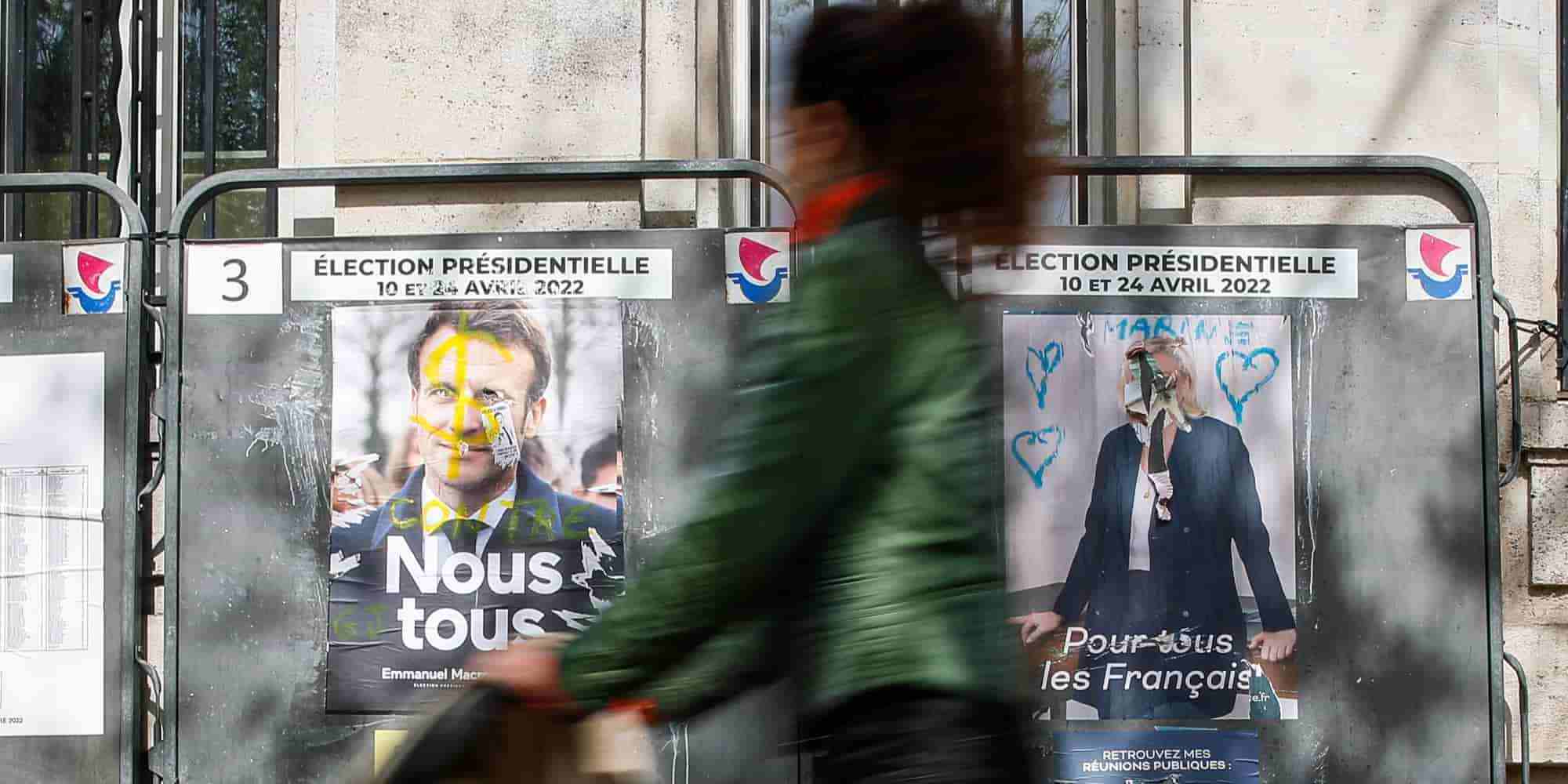 Γαλλίδα περνάει μπροστά από αφίσες με τον Εμανουέλ Μακρόν και την Μαρίν Λεπέν