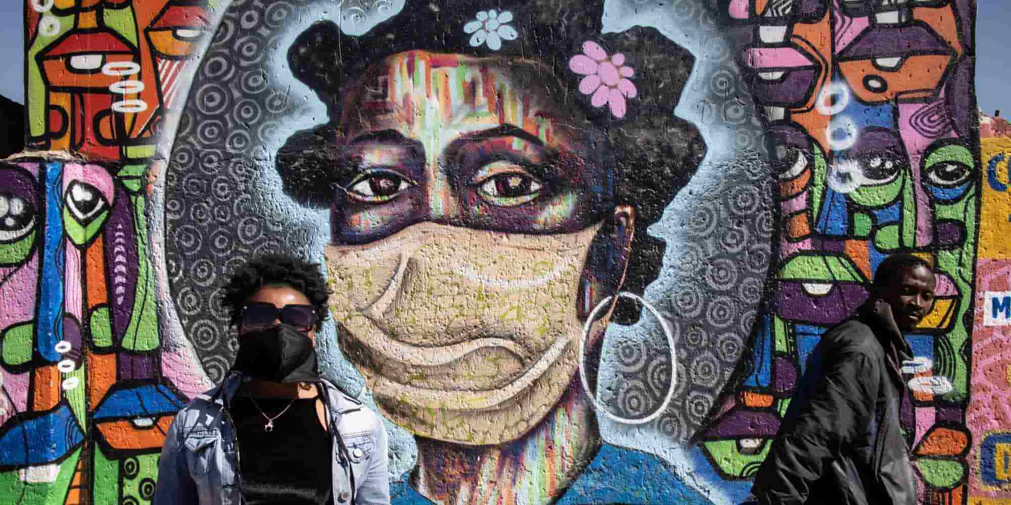 Δύο άνθρωποι με μάσκες στην Αφρική περνούν μπροστά από ένα γκράφιτι