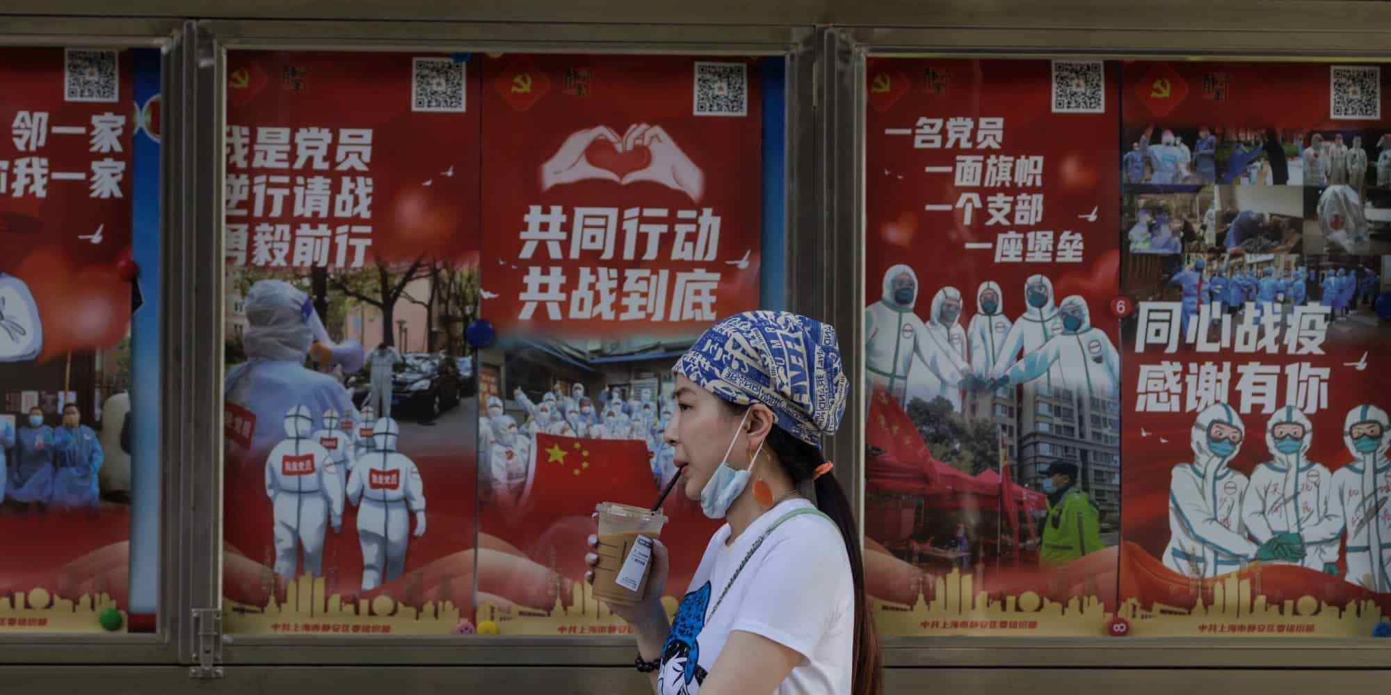 Μια γυναίκα περπατάει μπροστά από αφίσες για την πρόληψη του κορονoϊού στη Σαγκάη