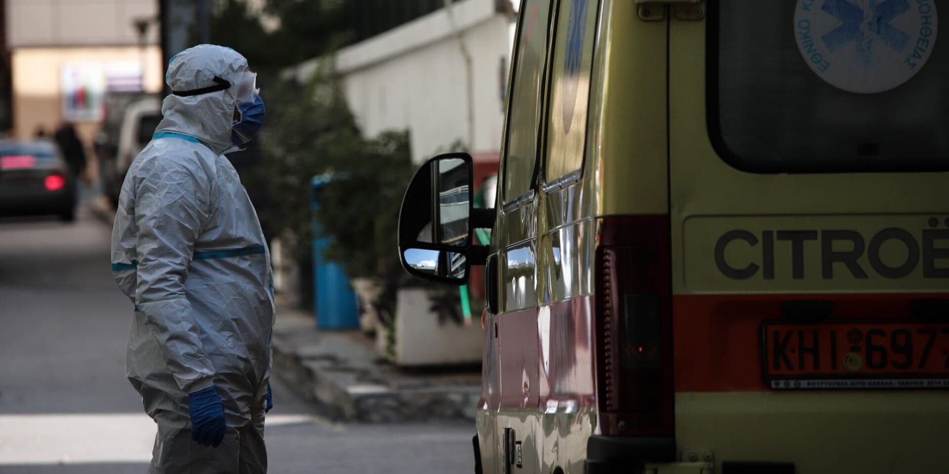 Ένας άνδρας με προστατευτική στολή μπροστά σε ασθενοφόρο
