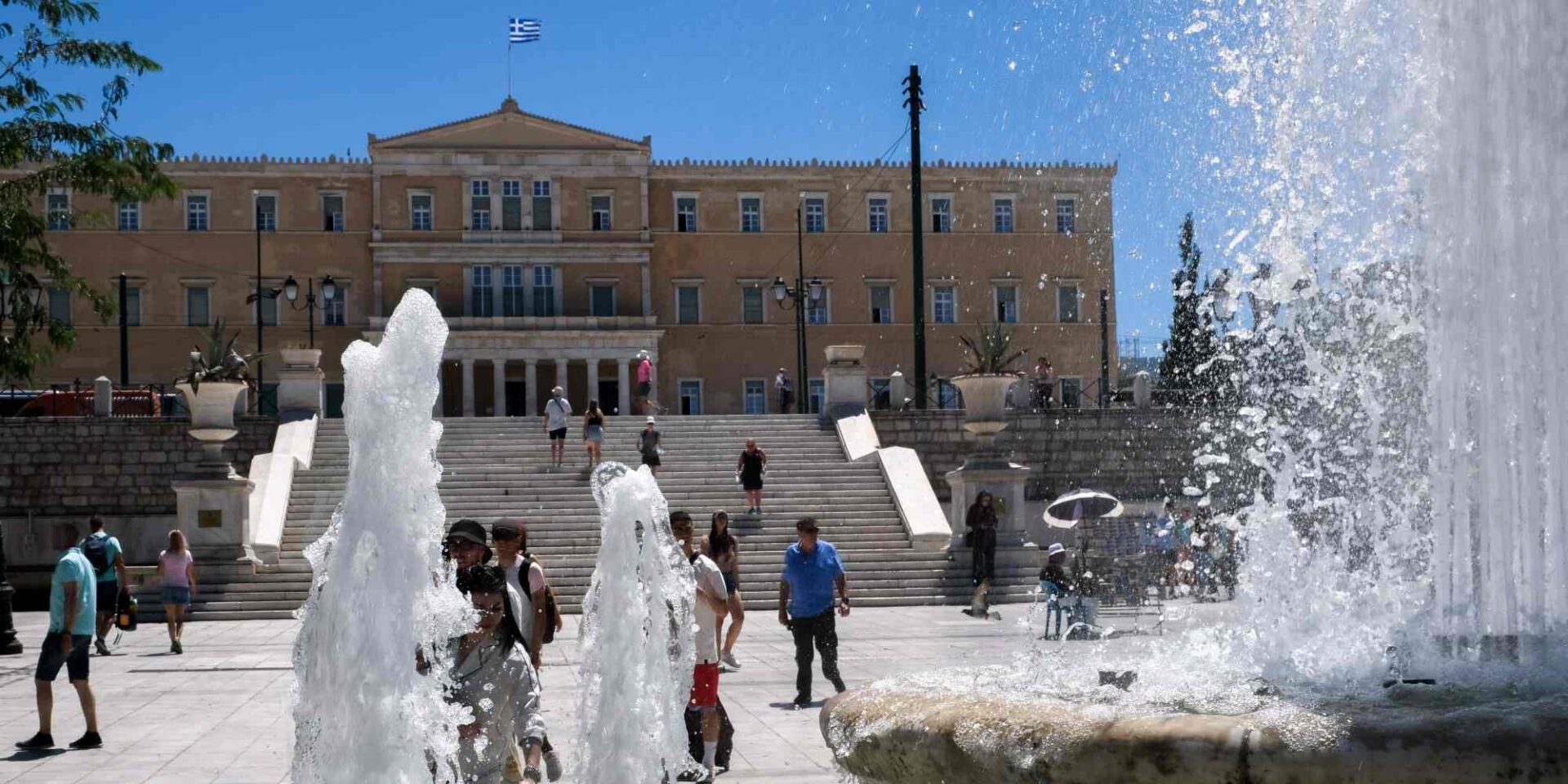 Κόσμος περπατά στην Πλατεία Συντάγματος μπροστά από τα σιντριβάνια