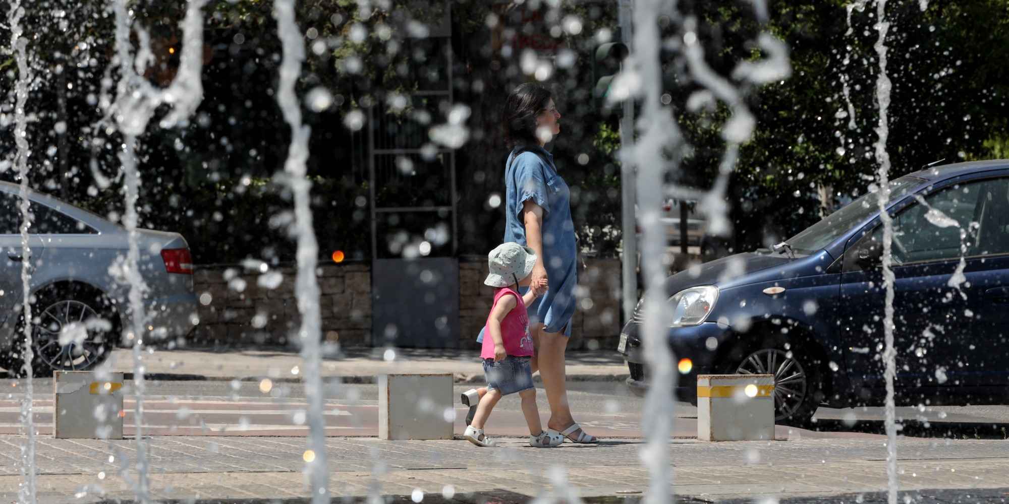 Μαμά με παιδί περνάει μπροστά από σιντριβάνι στο κέντρο της Αθήνας, εν μέσω καύσωνα