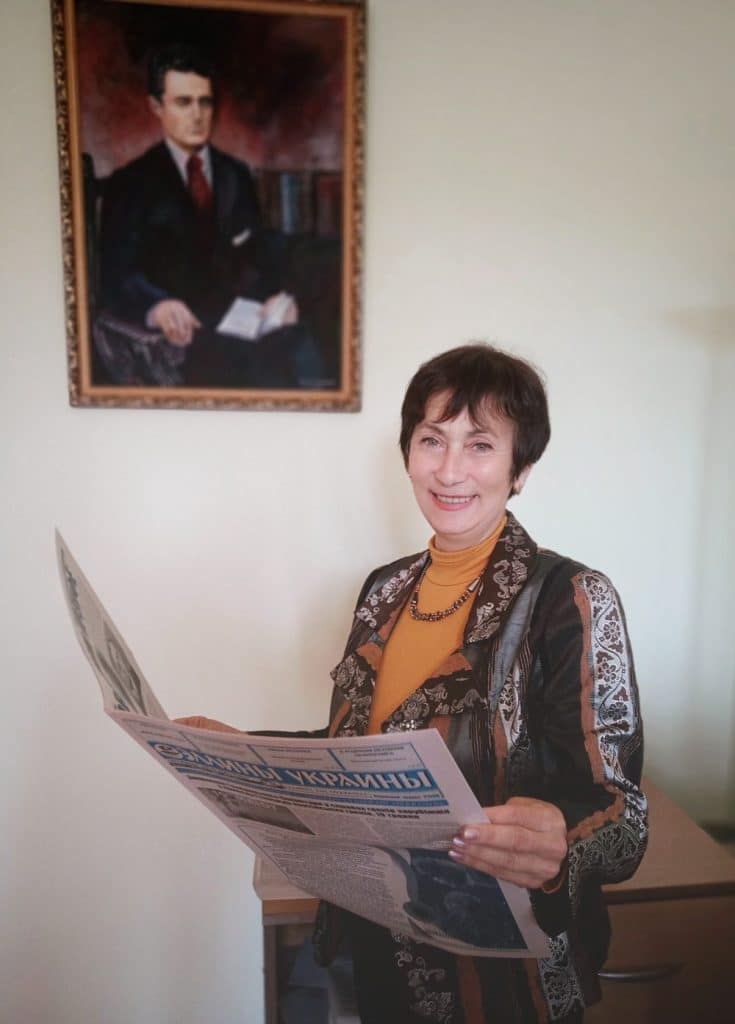 Η Νάντα Τσαπνή- Πρόεδρος του Ελληνικού Πολιτιστικού Κέντρου της Μαριούπολης στο γραφείο της εφημερίδας με φόντο το πορτρέτο του Γεώργιο Κοστοπράβ, εκδότη της πρώτης στην Μαριούπολη ελληνικής εφημερίδας «Κολλεκτιβιστής»