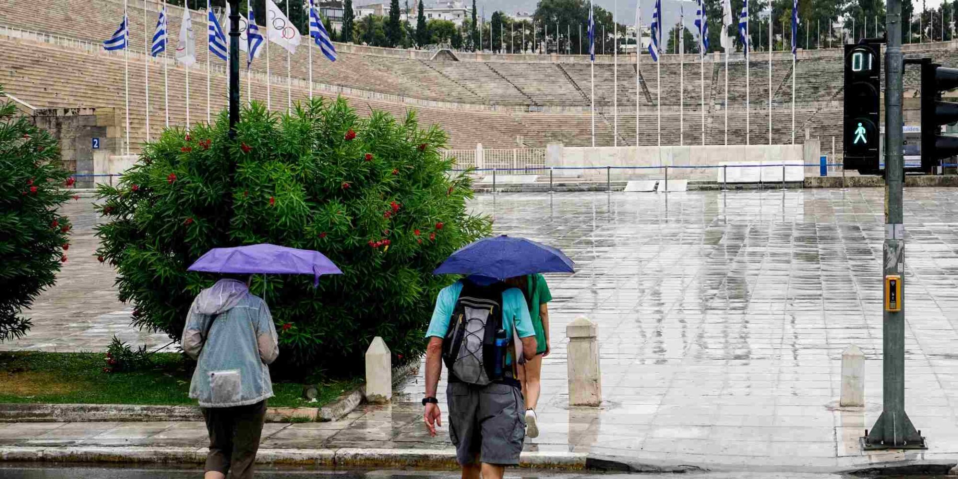 Πεζοί περπατούν με ομπρέλες στο Καλλιμάρμαρο Στάδιο