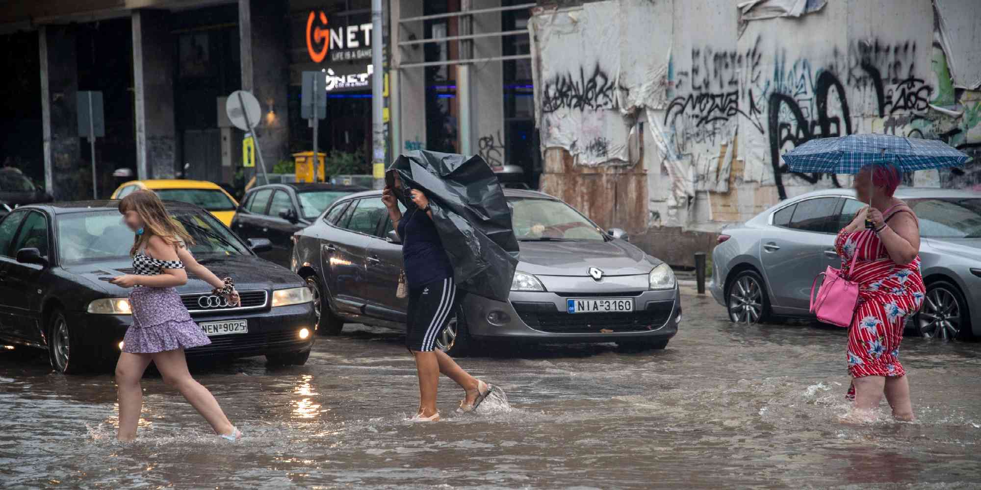 Άνθρωποι περπατούν σε πλημμυρισμένους δρόμους στην Θεσσαλονίκη μετά από καταιγίδα