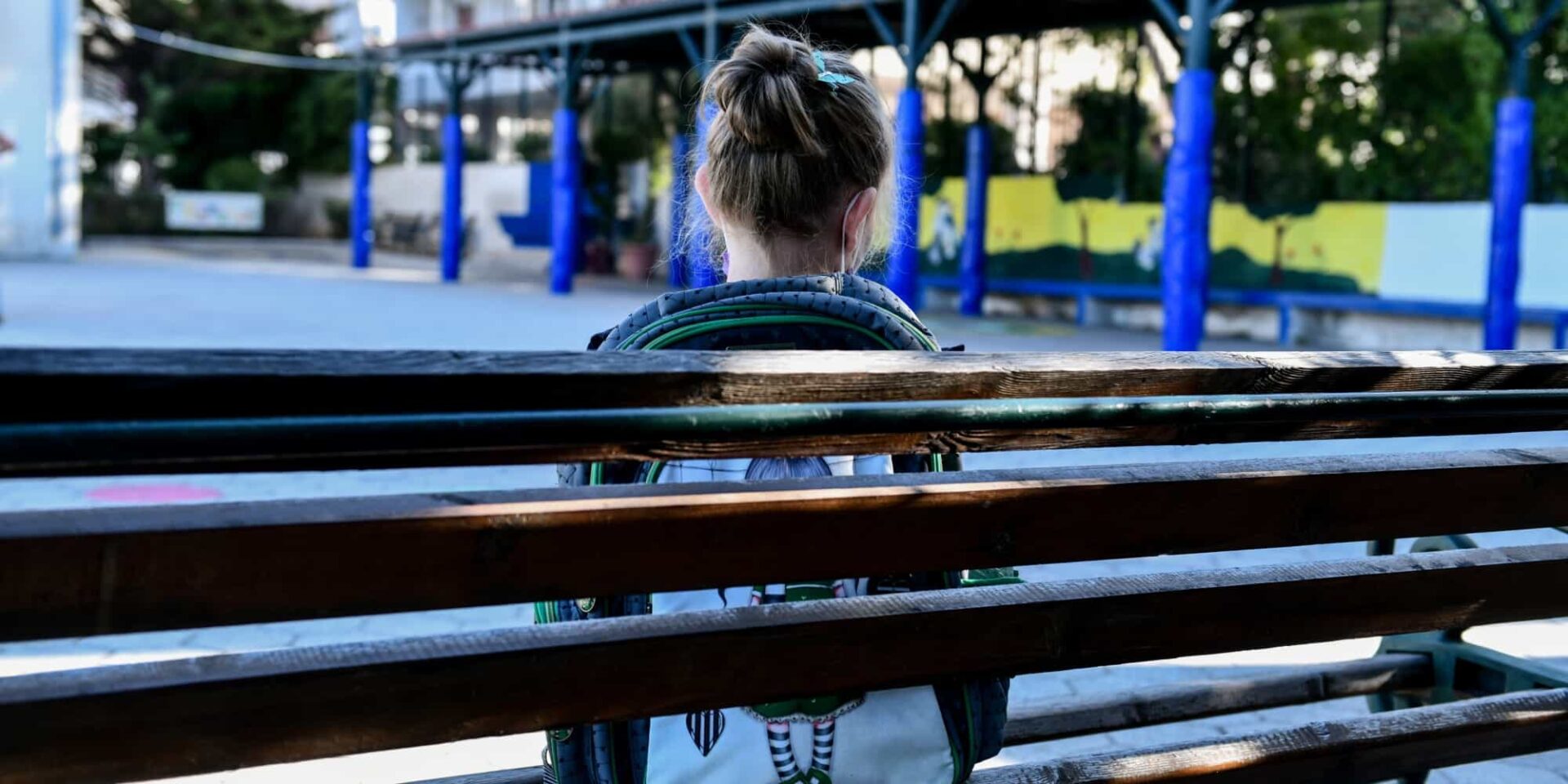 Μικρό κορίτσι κάθεται στο παγκάκι σχολείου