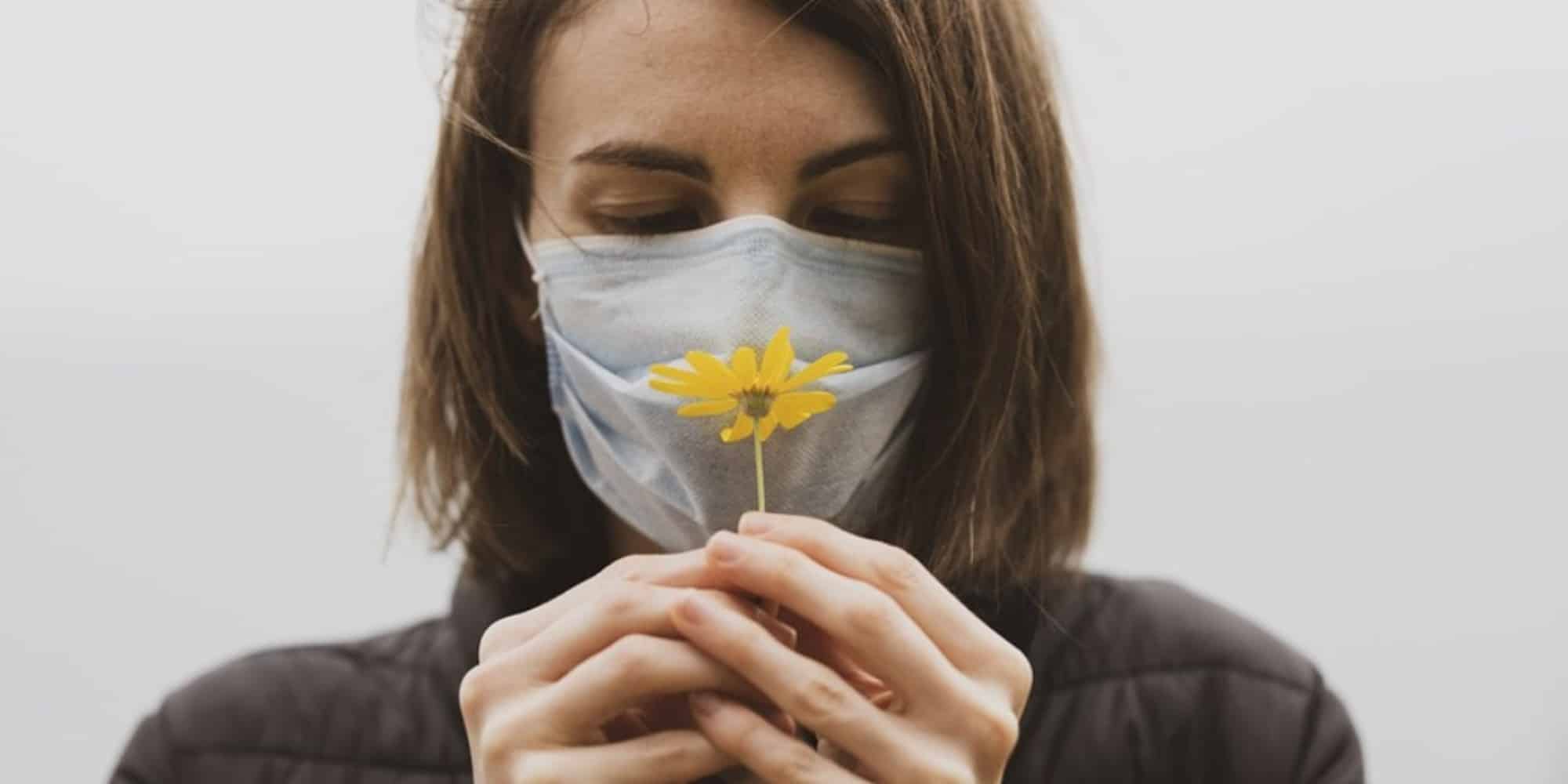 Γυναίκα μυρίζει λουλούδι φορώντας μάσκα
