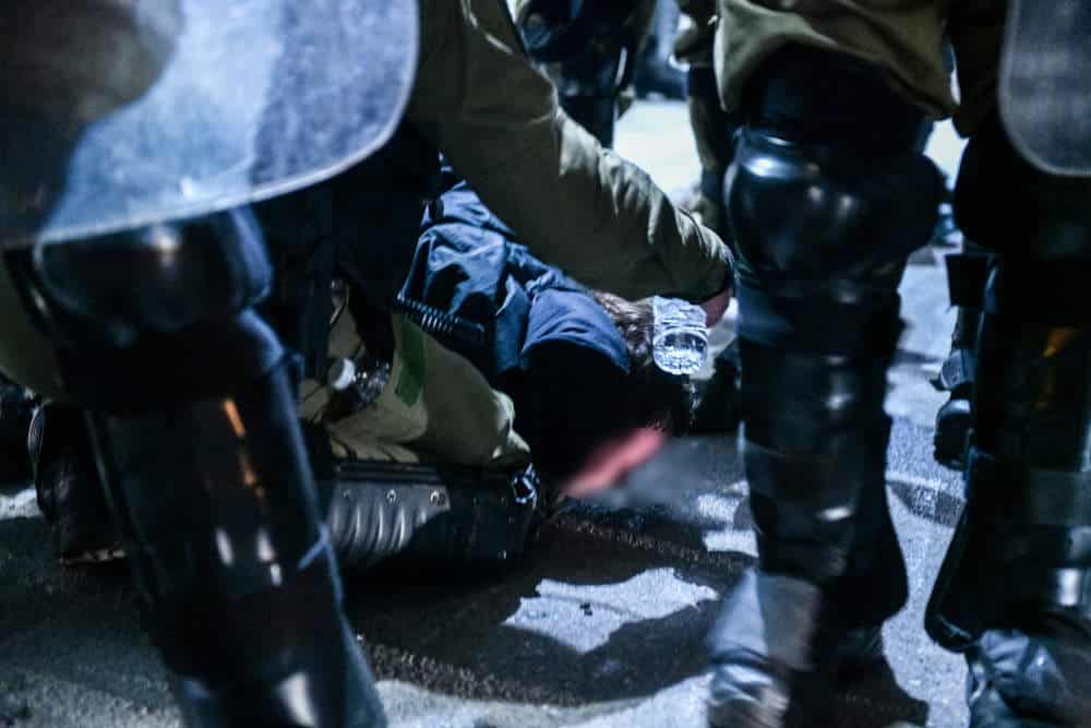 Διαδηλωτής στο έδαφος, του προσφέρουν νερό μετά από εκτεταμένη χρήση χημικών