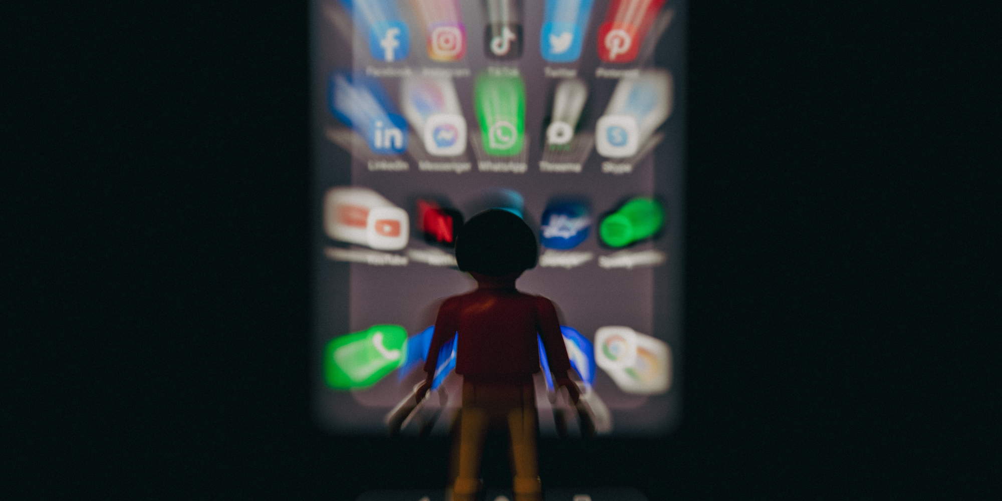 Playmobil μπροστά σε θολή εικόνα κινητού με τις εφαρμογές του TikTok, του Facebook, του Instagram και του YouTube