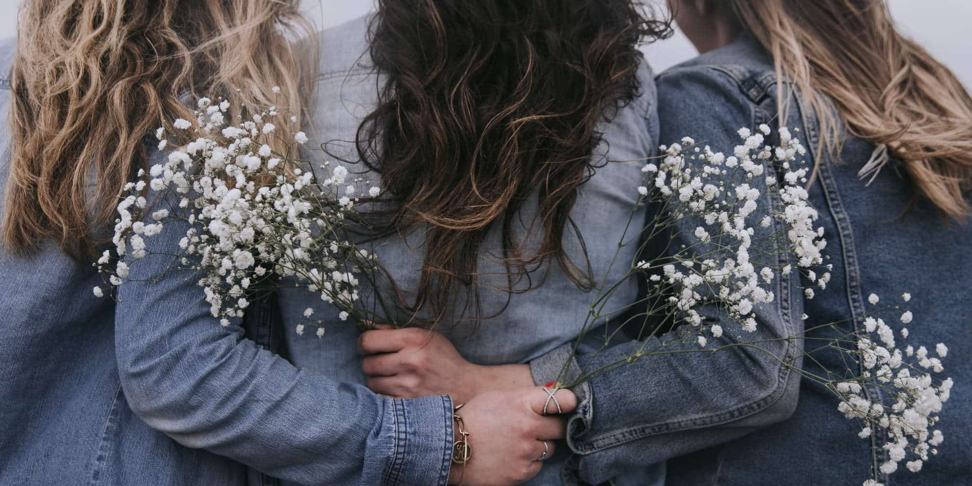 Γυναίκες που φορούν τζιν μπουφάν και κρατούν λουλούδια, αγκαλιασμένες / Φωτογραφία: Unsplash